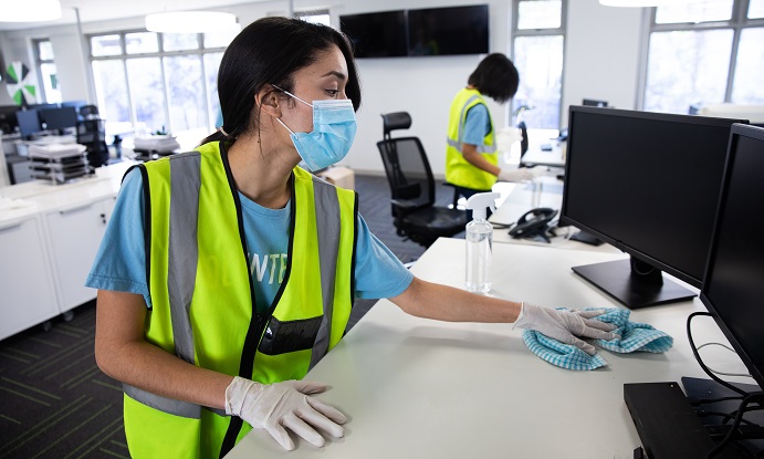 Woman wearing hi vis vest and face mask cleaning the office using disinfectant